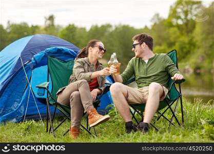 camping, travel, tourism, hike and people concept - happy couple clinking beer bottles at campsite tent