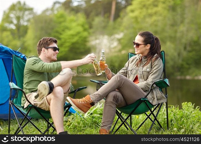 camping, travel, tourism, hike and people concept - happy couple clinking beer bottles at campsite tent