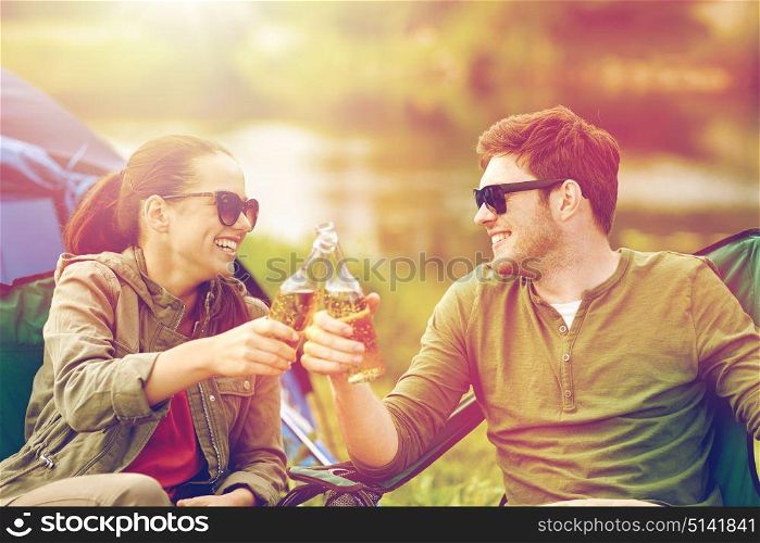 camping, travel, tourism, hike and people concept - happy couple clinking beer bottles at campsite tent. happy couple clinking drinks at campsite tent