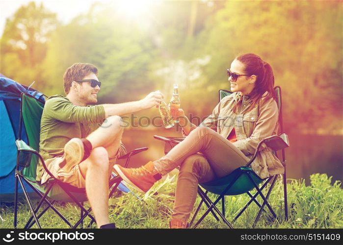 camping, travel, tourism, hike and people concept - happy couple clinking beer bottles at campsite tent. happy couple clinking drinks at campsite tent