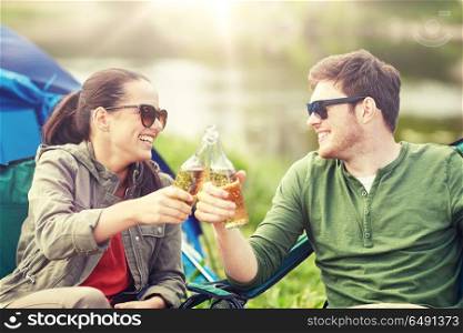 camping, travel, tourism, hike and people concept - happy couple clinking beer bottles at campsite tent. happy couple clinking drinks at campsite tent. happy couple clinking drinks at campsite tent