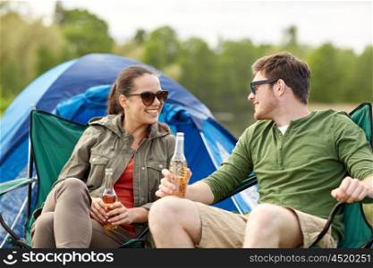 camping, travel, tourism, hike and people concept - happy couple drinking beer or cider at campsite tent