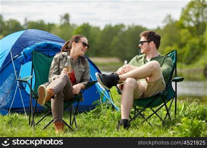 camping, travel, tourism, hike and people concept - happy couple drinking beer or cider at campsite tent