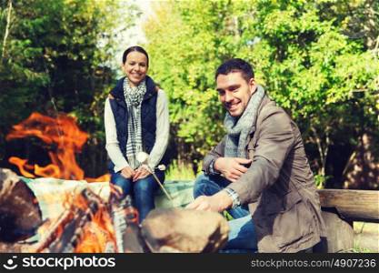 camping, travel, tourism, hike and people concept - happy couple roasting marshmallow over campfire at camp in woods. happy couple roasting marshmallow over camp fire