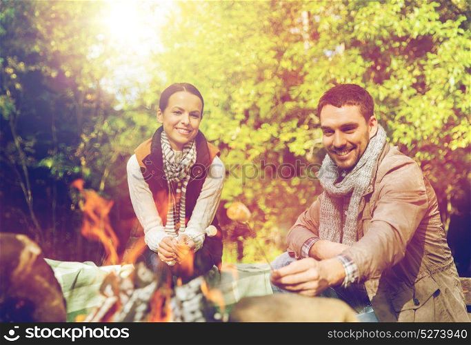 camping, travel, tourism, hike and people concept - happy couple roasting marshmallow over campfire at camp in woods. happy couple roasting marshmallow over camp fire