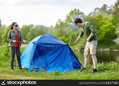 camping, travel, tourism, hike and people concept - happy couple setting up tent outdoors