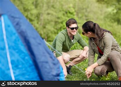 camping, travel, tourism, hike and people concept - happy couple setting up tent outdoors