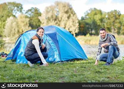 camping, travel, tourism, hike and people concept - happy couple setting up tent outdoors