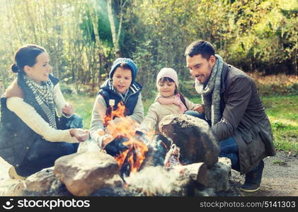 camping, travel, tourism, hike and people concept - happy family roasting marshmallow over campfire. happy family roasting marshmallow over campfire