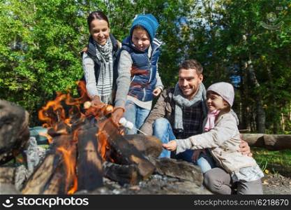 camping, travel, tourism, hike and people concept - happy family roasting marshmallow over campfire