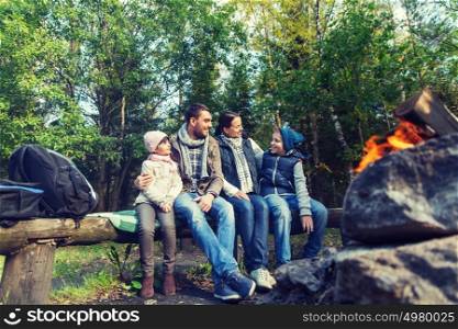 camping, travel, tourism, hike and people concept - happy family sitting on bench and talking at camp near campfire in woods. happy family sitting on bench at camp fire