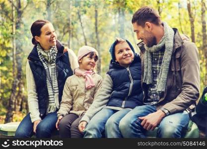camping, travel, tourism, hike and people concept - happy family sitting on bench and talking at camp in woods. happy family sitting on bench and talking at camp. happy family sitting on bench and talking at camp