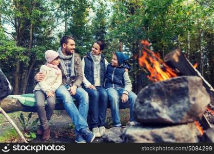 camping, travel, tourism, hike and people concept - happy family sitting on bench and talking at camp near campfire in woods. happy family sitting on bench at camp fire. happy family sitting on bench at camp fire