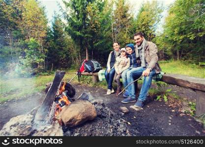 camping, travel, tourism, hike and people concept - happy family sitting on bench at camp fire in woods. happy family sitting on bench at camp fire