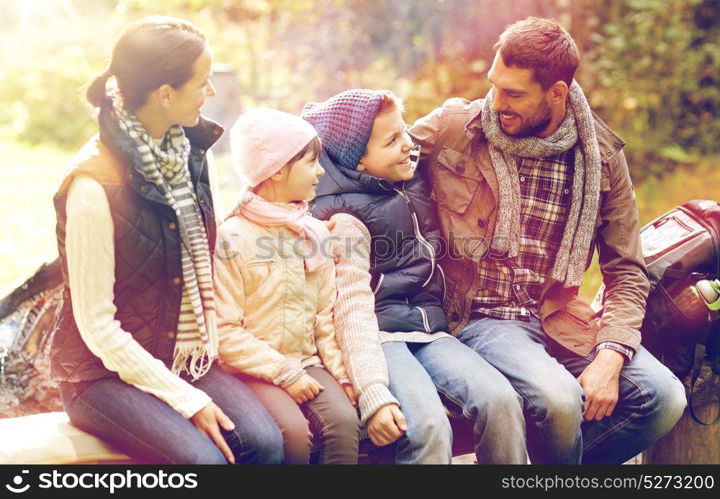 camping, travel, tourism, hike and people concept - happy family sitting on bench and talking at camp in woods. happy family sitting on bench and talking at camp