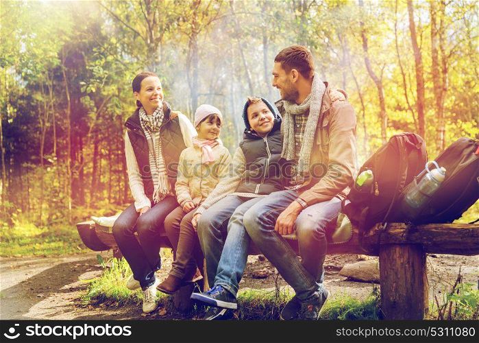 camping, travel, tourism, hike and people concept - happy family sitting on bench and talking at camp in woods. happy family sitting on bench and talking at camp