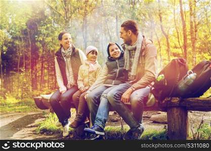 camping, travel, tourism, hike and people concept - happy family sitting on bench and talking at camp in woods. happy family sitting on bench and talking at camp