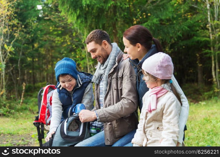 camping, travel, tourism, hike and people concept - happy family with backpacks and thermos at camp
