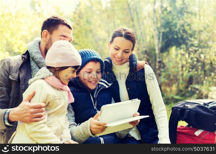 camping, travel, tourism, hike and people concept - happy family with tablet pc computer and backpacks at camp in woods. happy family with tablet pc and backpacks at camp