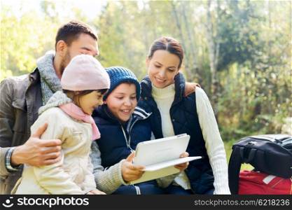 camping, travel, tourism, hike and people concept - happy family with tablet pc computer and backpacks at camp in woods