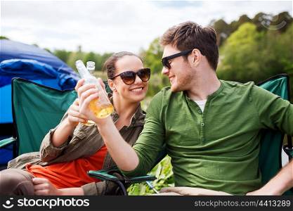 camping, travel, tourism, hike and people concept - happy friends clinking glass bottles and drinking cider or beer at campsite
