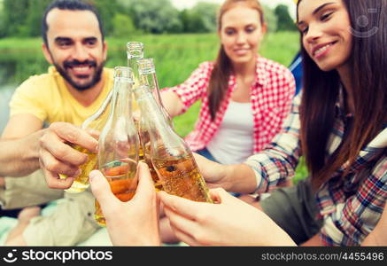 camping, travel, tourism, hike and people concept - happy friends clinking glass bottles and drinking cider or beer at campsite