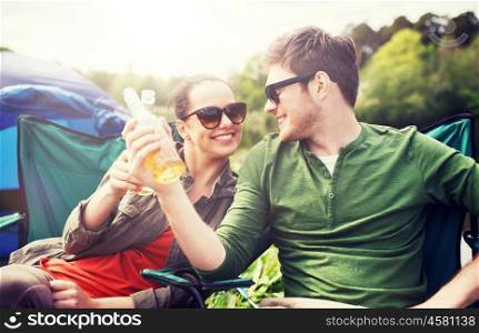 camping, travel, tourism, hike and people concept - happy friends clinking glass bottles and drinking cider or beer at campsite. happy couple clinking drinks at campsite tent. happy couple clinking drinks at campsite tent