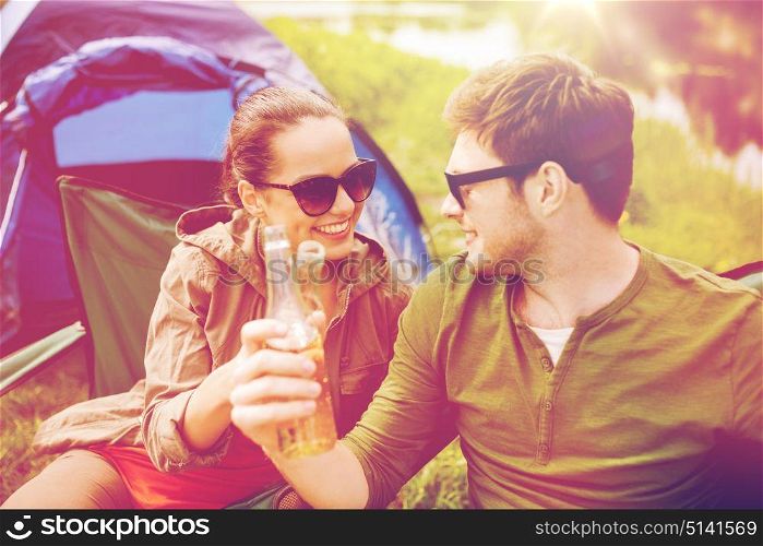 camping, travel, tourism, hike and people concept - happy friends clinking glass bottles and drinking cider or beer at campsite. happy couple clinking drinks at campsite tent