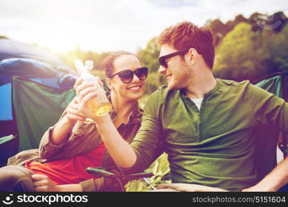 camping, travel, tourism, hike and people concept - happy friends clinking glass bottles and drinking cider or beer at campsite. happy couple clinking drinks at campsite tent