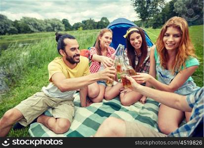 camping, travel, tourism, hike and people concept - happy friends with glass bottles drinking cider or beer at campsite