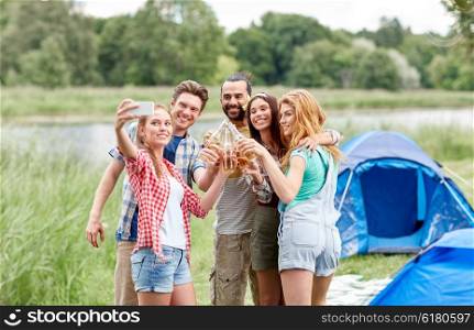 camping, travel, tourism, hike and people concept - happy friends with glass bottles drinking cider or beer and taking selfie by smartphone at camping