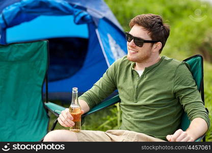 camping, travel, tourism, hike and people concept - happy young man drinking beer at campsite tent