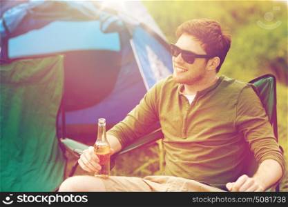 camping, travel, tourism, hike and people concept - happy young man drinking beer at campsite tent. happy young man drinking beer at campsite tent