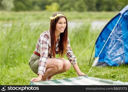 camping, travel, tourism, hike and people concept - happy young woman laying blanket at campsite