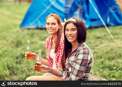 camping, travel, tourism, hike and people concept - happy young women with glass bottles drinking cider or beer at campsite