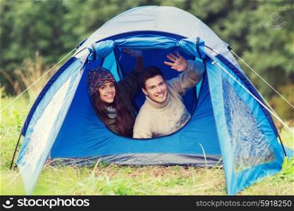 camping, travel, tourism, hike and people concept - smiling couple of tourists looking out from tent and waving hands