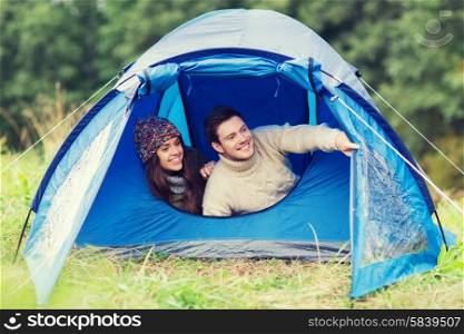 camping, travel, tourism, hike and people concept - smiling couple of tourists looking out from tent