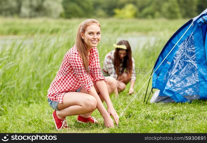 camping, travel, tourism, hike and people concept - smiling friends setting up tent outdoors