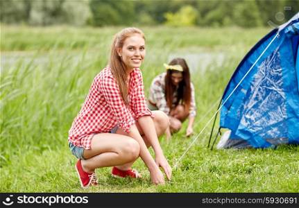 camping, travel, tourism, hike and people concept - smiling friends setting up tent outdoors