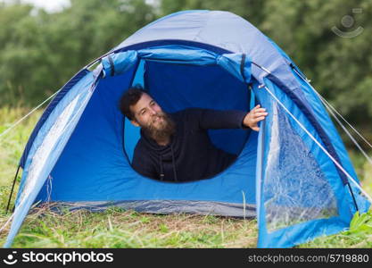 camping, travel, tourism, hike and people concept - smiling male tourist with beard in tent