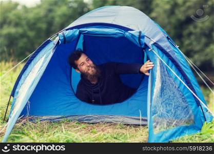 camping, travel, tourism, hike and people concept - smiling male tourist with beard in tent