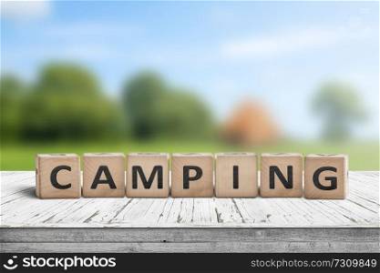 Camping word on a wooden cube sign with a blurry background of a campsite in the summer