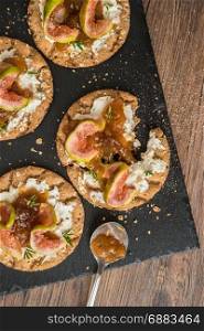 Canape or crostini with multigrain crispread with cream cheese and fig jam on a slate board. Delicious appetizer ideal as an aperitif.