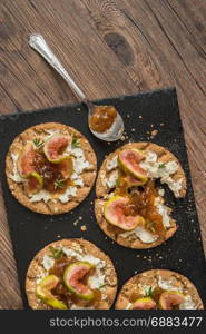 Canape or crostini with multigrain crispread with cream cheese and fig jam on a slate board. Delicious appetizer ideal as an aperitif.