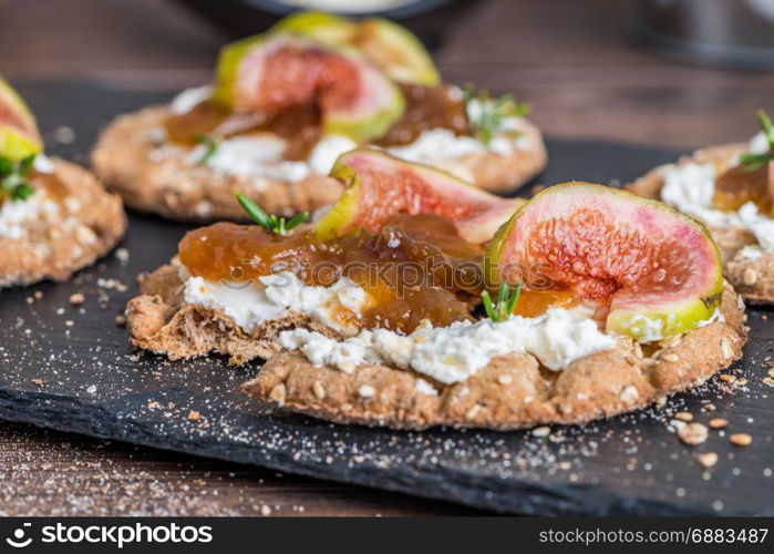 Canape or crostini with multigrain crispread with cream cheese and fig jam on a slate board. Delicious appetizer ideal as an aperitif.