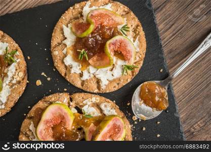 Canape or crostini with multigrain crispread with cream cheese and fig jam on a slate board. Delicious appetizer ideal as an aperitif.