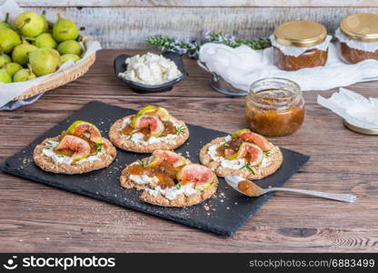 Canape or crostini with multigrain crispread with cream cheese and fig jam on a slate board. Delicious appetizer ideal as an aperitif.