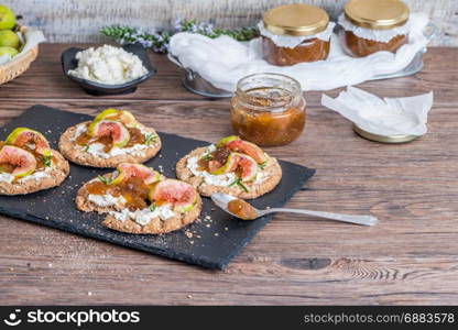 Canape or crostini with multigrain crispread with cream cheese and fig jam on a slate board. Delicious appetizer ideal as an aperitif.