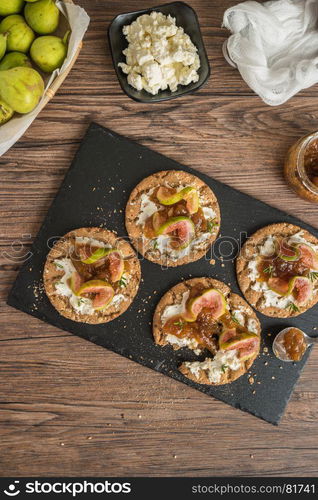 Canape or crostini with multigrain crispread with cream cheese and fig jam on a slate board. Delicious appetizer ideal as an aperitif.