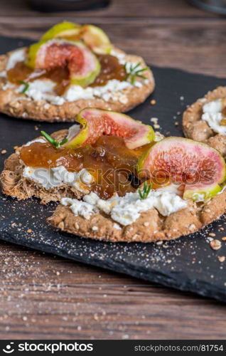 Canape or crostini with multigrain crispread with cream cheese and fig jam on a slate board. Delicious appetizer ideal as an aperitif.